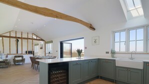 A spacious kitchen with a large island, wooden beams, and a view to the outside. - The Hide (Colchester)