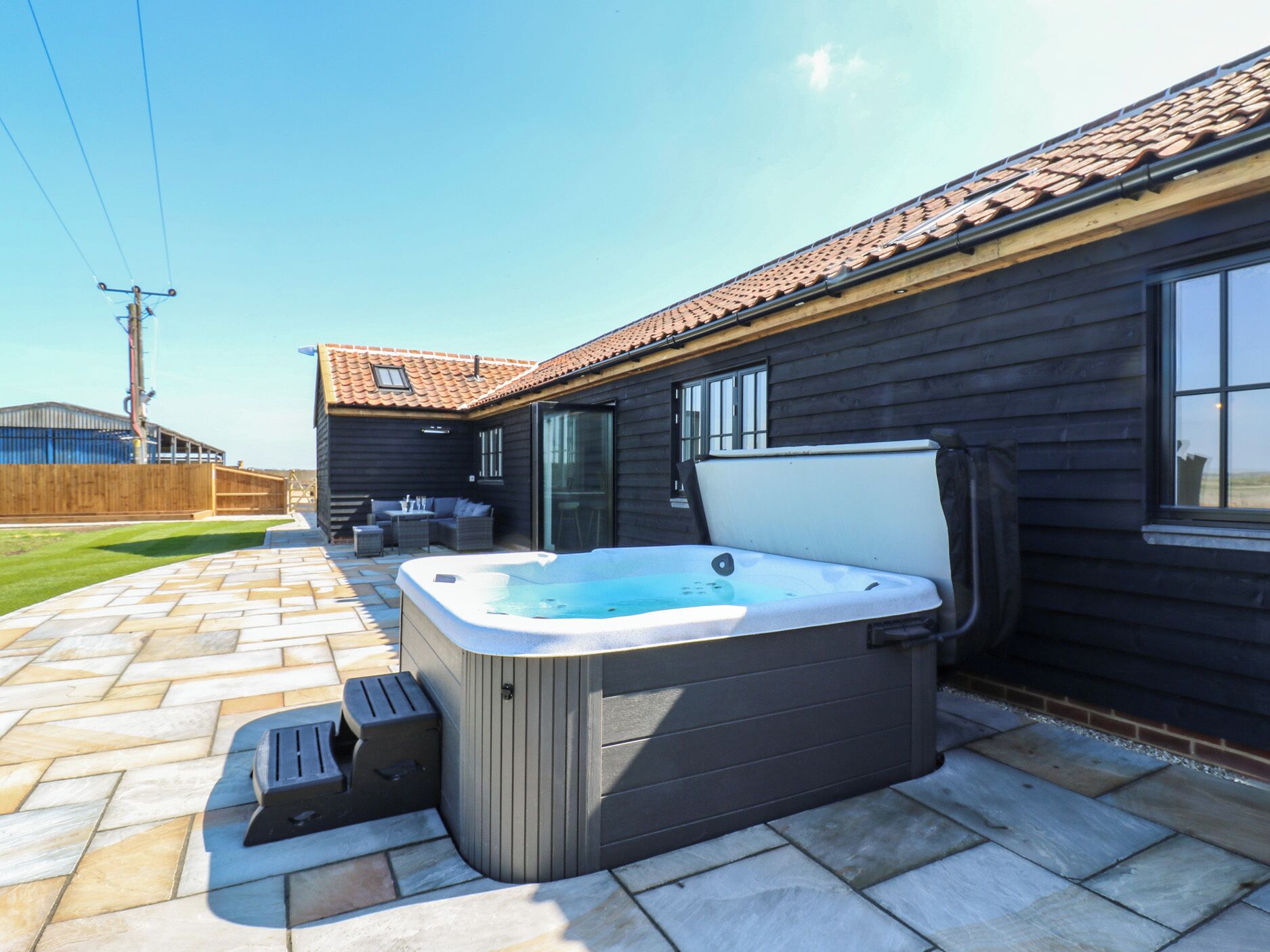 Een bubbelbad in een achtertuin met een terras, houten terras en een huis met een pannendak.