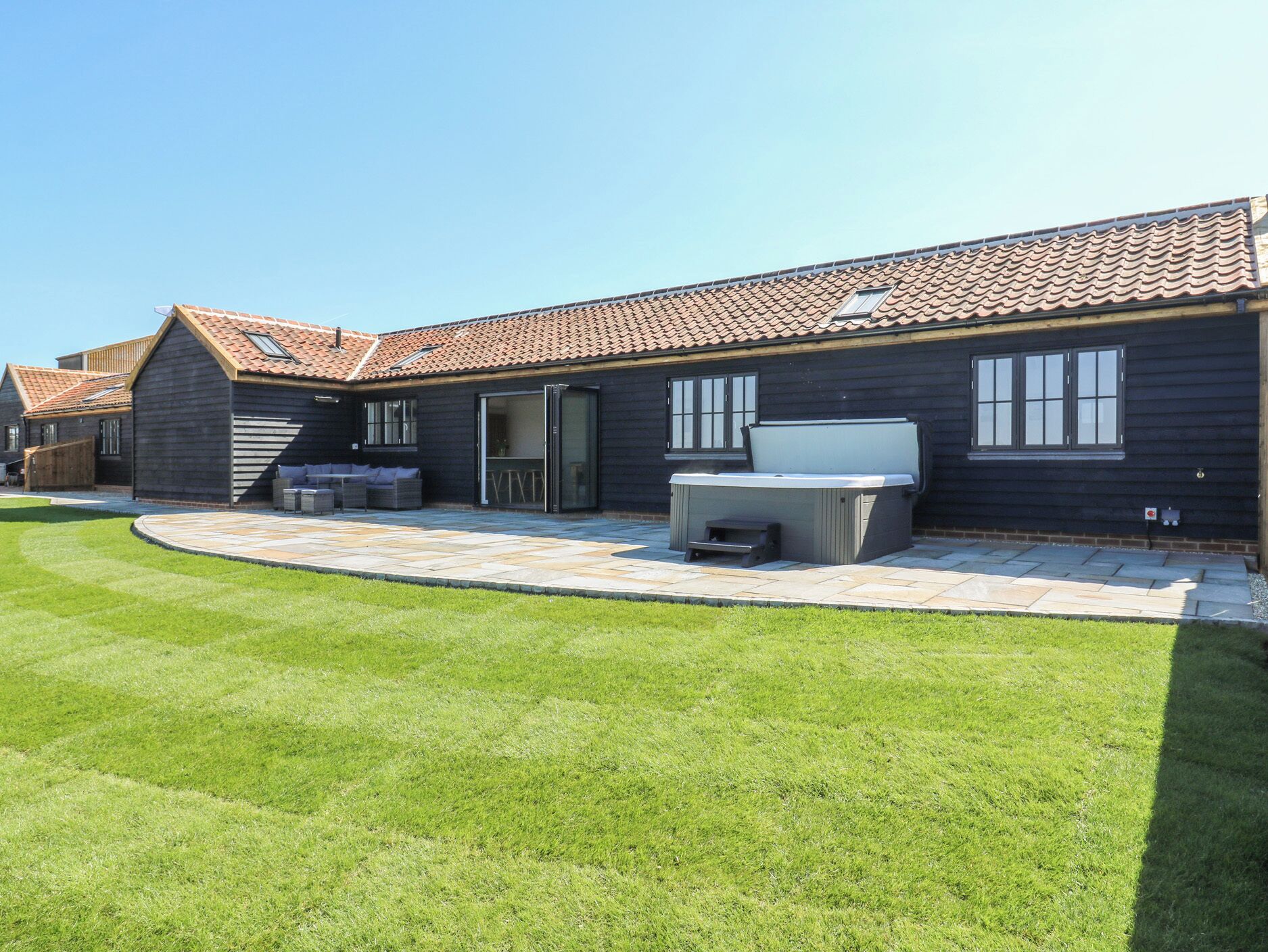 Et moderne hus med terrasse, jacuzzi og en velplejet græsplæne.