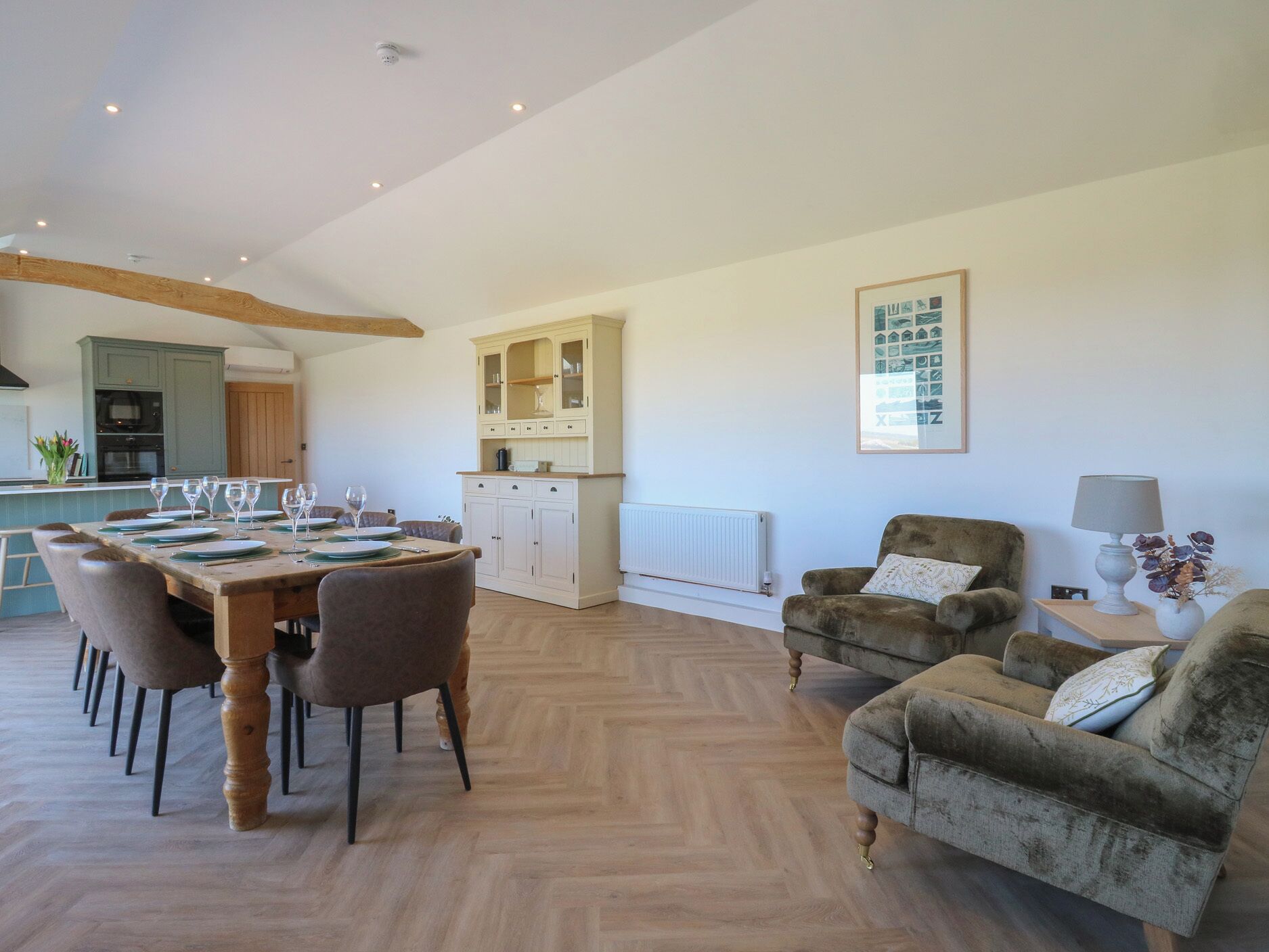 A spacious living area with a dining table set for six, a sofa, and a cabinet with glass doors.