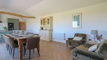 A spacious living area with a dining table set for six, a sofa, and a cabinet with glass doors.