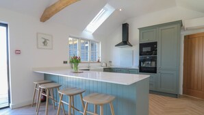A kitchen with a central island, bar stools, a window, and a built-in oven. - The Hide (Colchester)