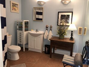 Une salle de bain comprenant des toilettes, un lavabo, un meuble de rangement et une petite table avec une lampe et une plante.