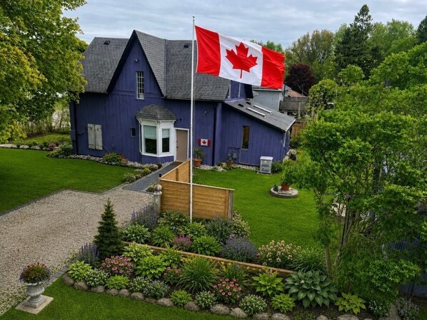 Une maison à deux étages, ornée d’un mât pour drapeau, dotée d’une pelouse bien entretenue et agrémentée de diverses plantes.