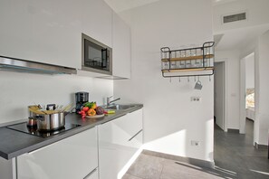 Una cocina moderna con una campana extractora de acero inoxidable, un microondas empotrado y una isla con placa de vidrio y utensilios de cocina.