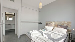 Quarto moderno com cama bem arrumada, mesa de cabeceira e luminária pendente.