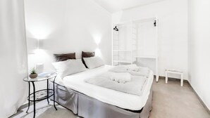 Une chambre à coucher moderne avec un lit, des tables de chevet, une petite table avec une plante et une étagère fixée au mur.