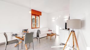 A modern living room with a dining area, white walls, and a large window.