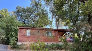 Une petite cabane en bois, portant le numéro « 102 » sur le côté, entourée d’une végétation luxuriante et d’arbres.