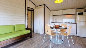 Un espace de vie compact comprenant un canapé vert, une table à manger avec des chaises, un coin cuisine avec des placards et des appareils électroménagers, et un plafond en bois.