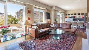Een moderne woonkamer met een bruine leren bank, een glazen salontafel en een kamerkleed met dessin.
