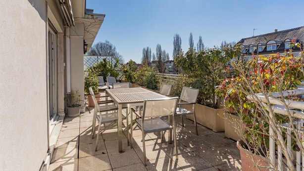 Een terras buiten met een tafel en stoelen, omringd door plantenpotten en uitzicht op de buurt.