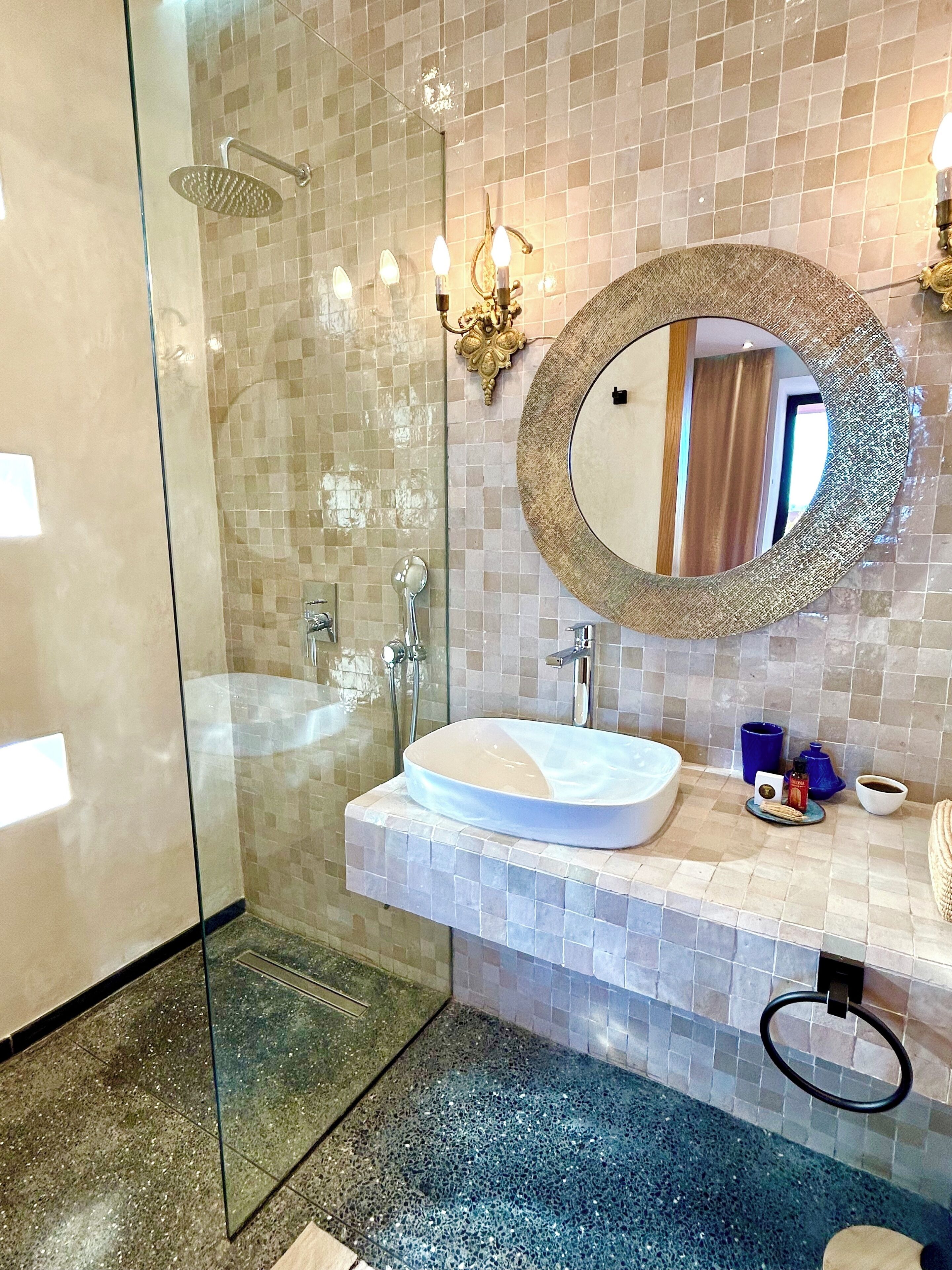 A modern bathroom with a glass-enclosed shower, a white sink with a round mirror, and a tiled backsplash.