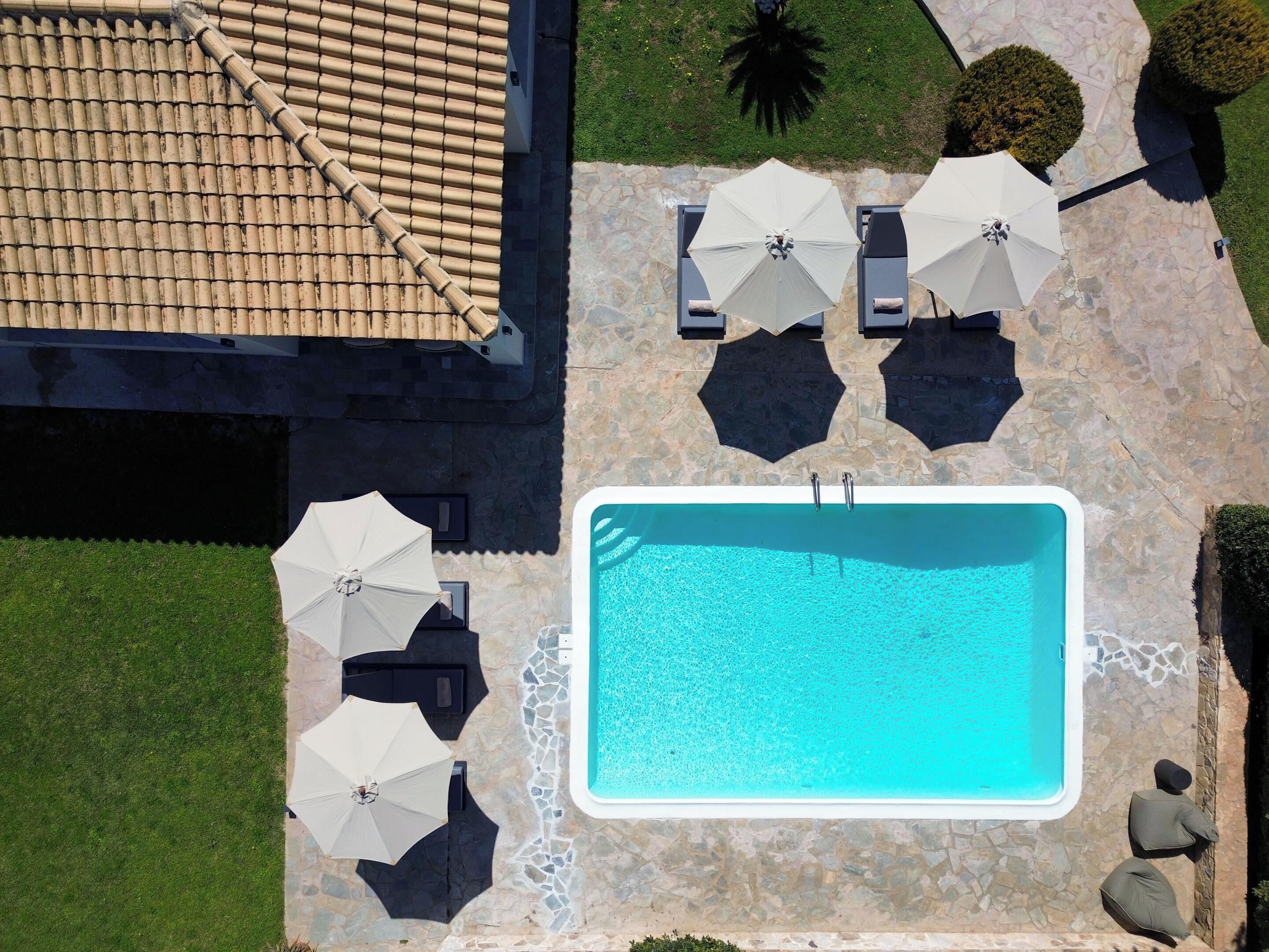An aerial view of a swimming pool area with a tiled roof, stone flooring, and multiple umbrellas.