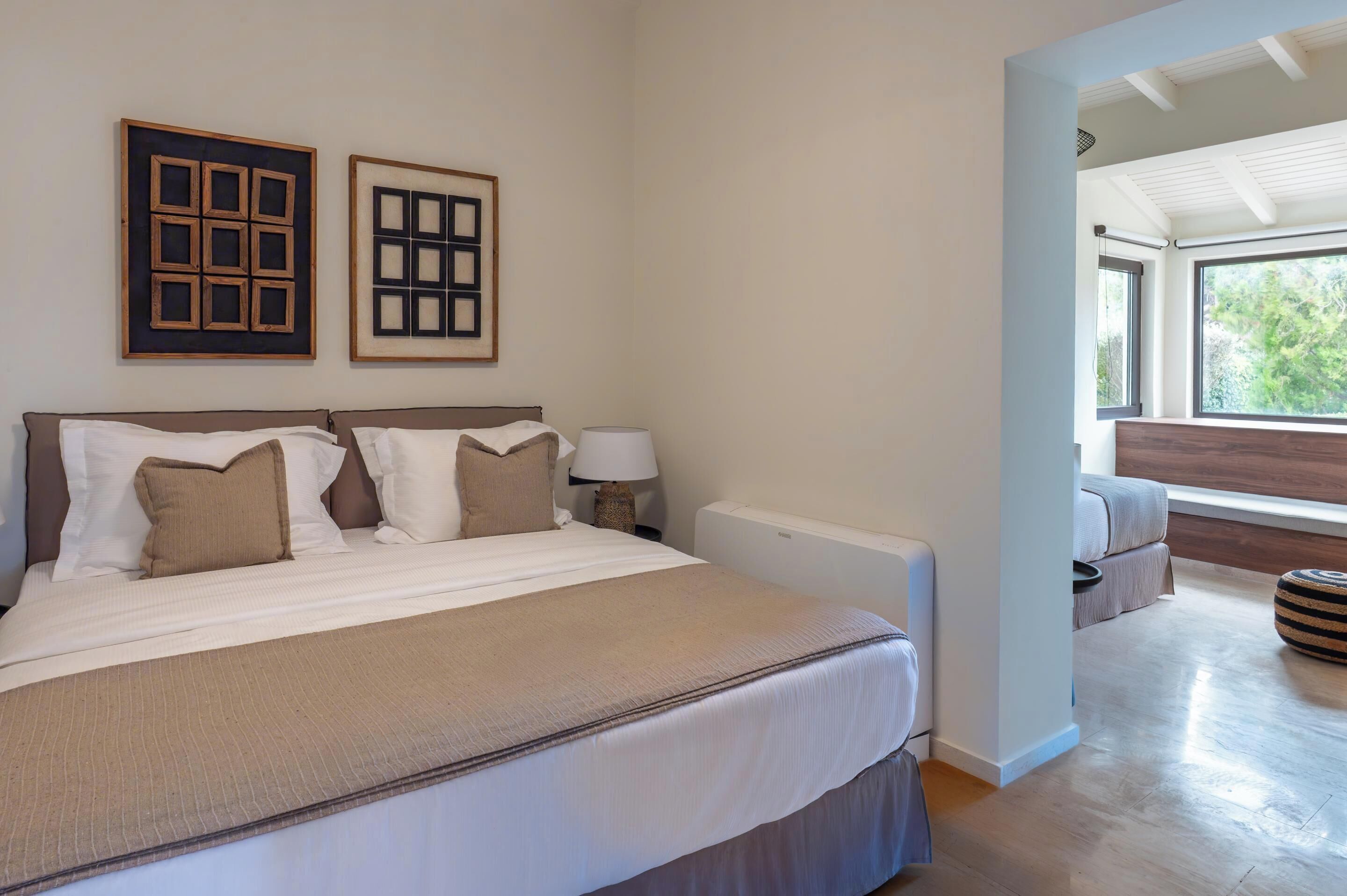 A bedroom with a large bed, two bedside tables, a nightstand, and a window with a view of greenery.