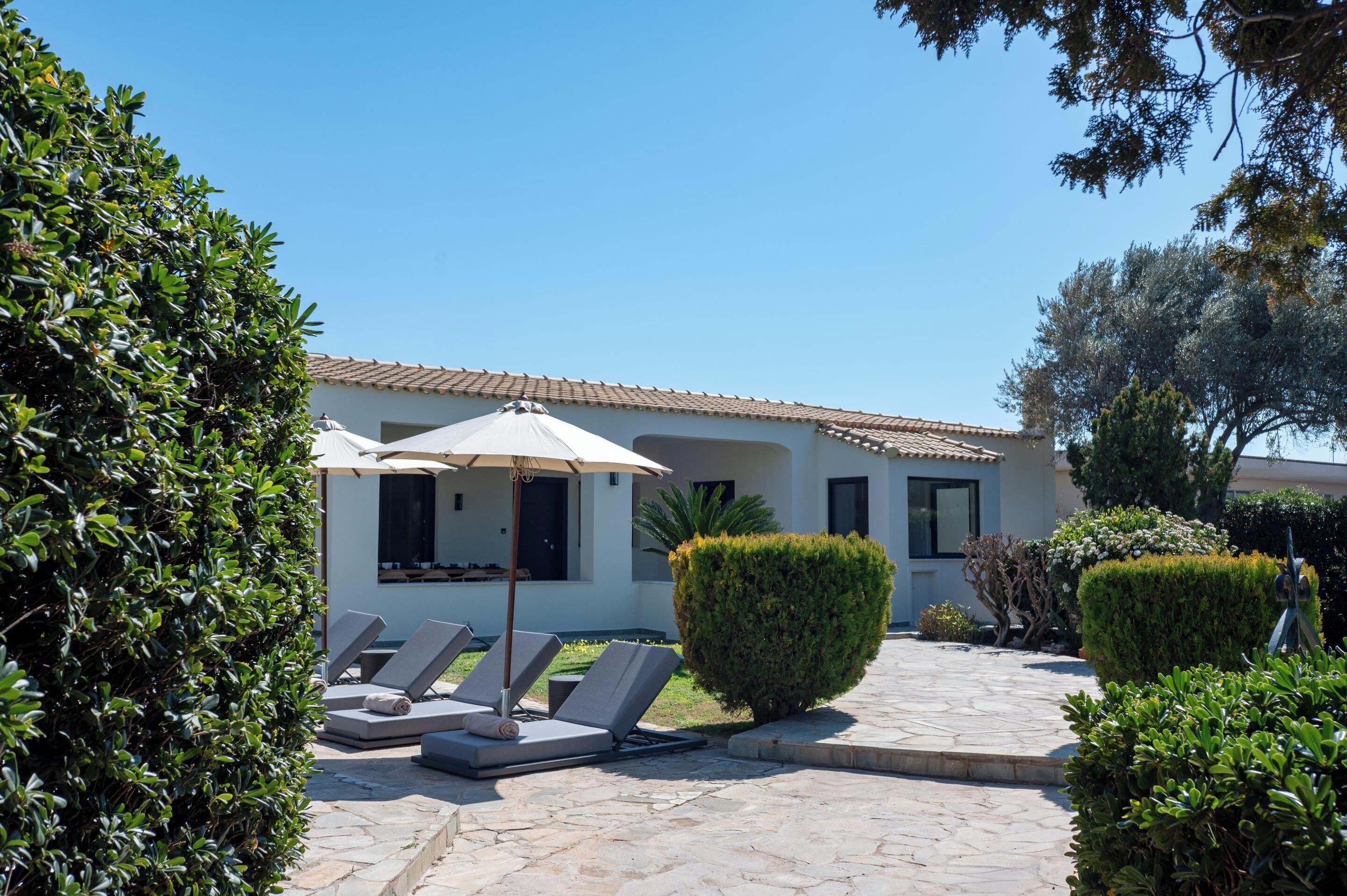 A modern building with a tiled roof, a pool area with lounge chairs and umbrellas, and well-maintained landscaping.