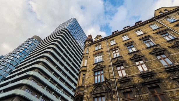 Een modern hoog gebouw met een gebogen gevel en een traditioneel bakstenen gebouw met veel ramen en een hoektorentje.