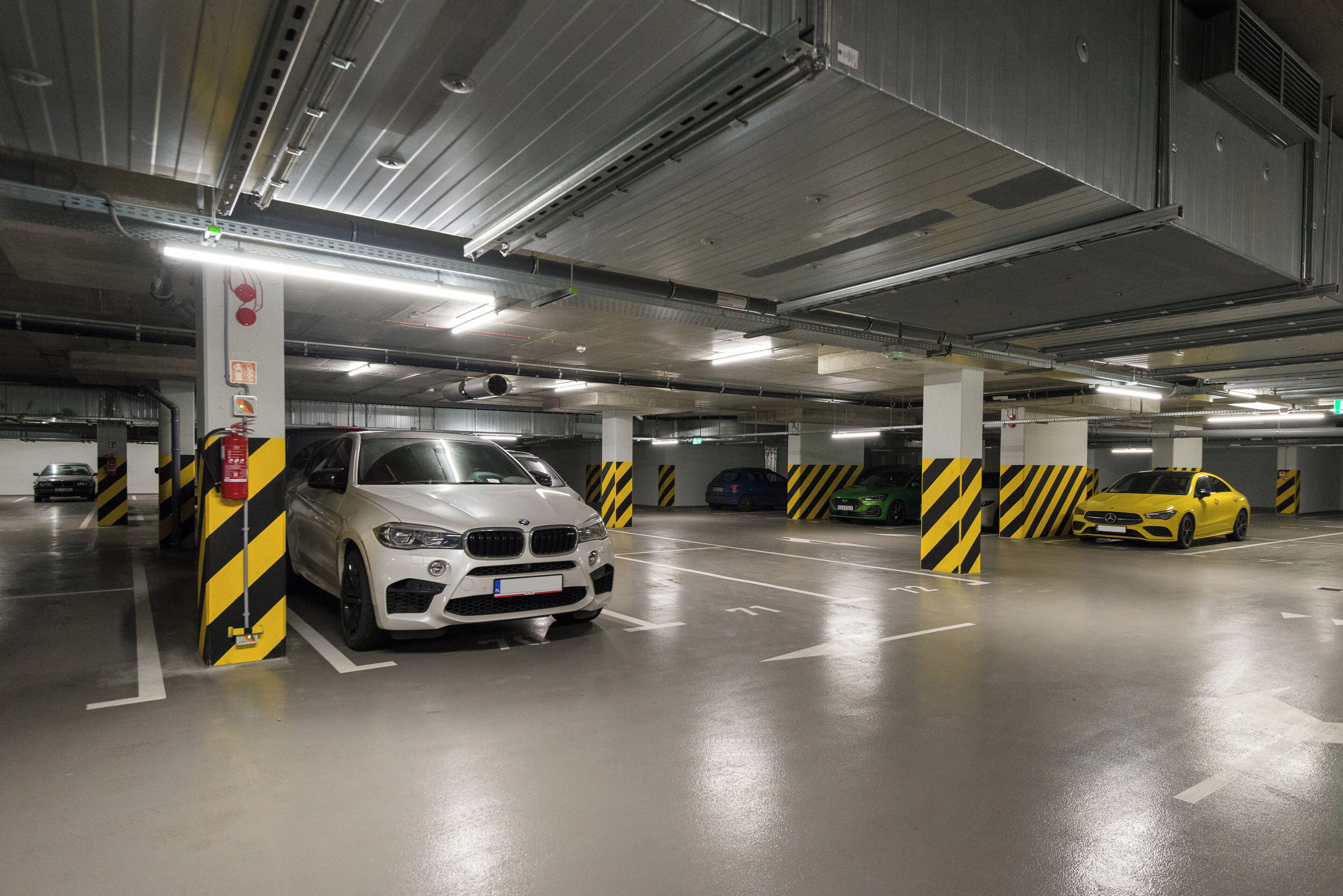 A multi-level parking garage with cars parked in designated spaces, fire extinguishers, and safety signage.