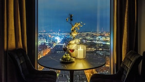 A table with a vase, candle, and wine glass, set against a cityscape view through a window with curtains. - Apartament Bulvar - by Kairos Apartments (Katowice)