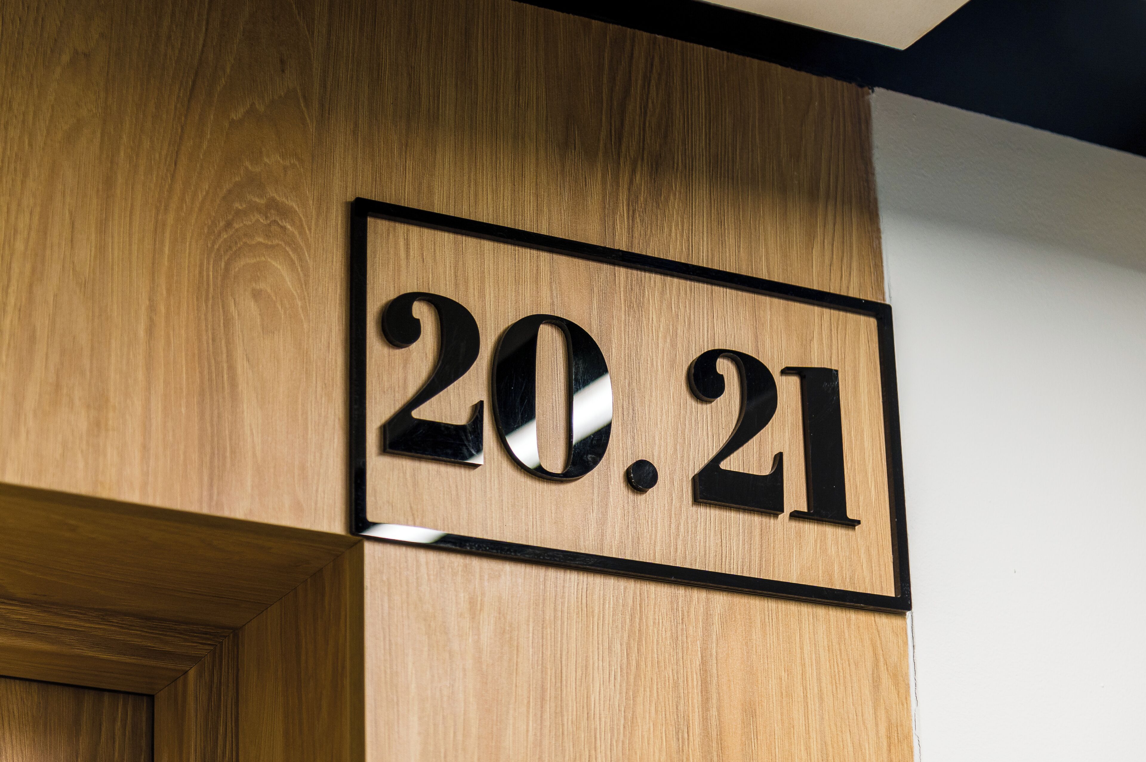 Een houten muur met een zwart omlijst bord waarop de cijfers '20.21' staan.