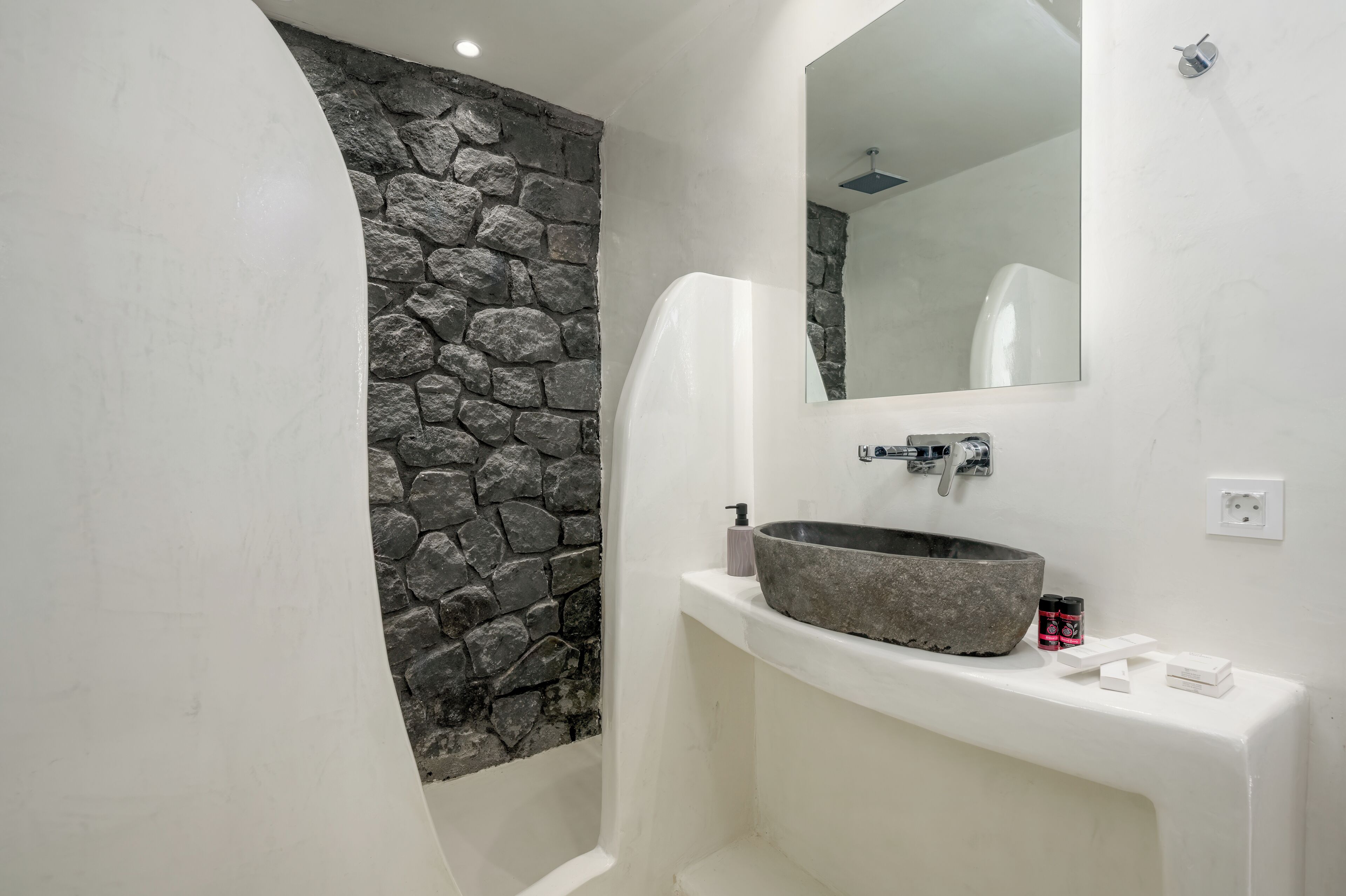 Ein Badezimmer mit Steinwand, großem Spiegel, Waschbecken und weißem Waschtisch.
