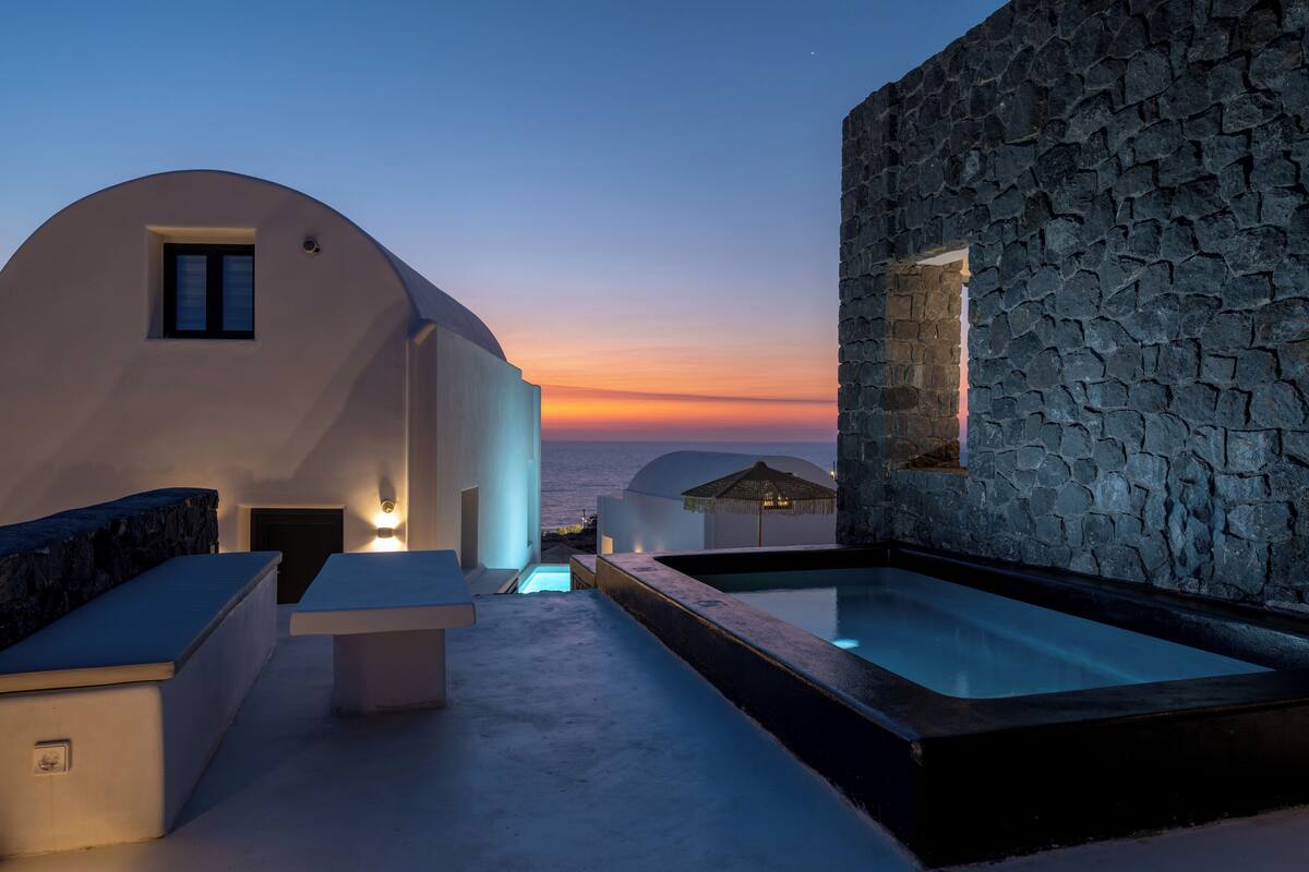 Un espace piscine extérieur moderne, avec un mur en pierre et un bâtiment blanc doté d’une petite fenêtre.