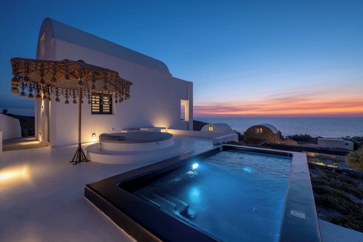 Un espace piscine extérieur moderne offrant une vue sur le coucher du soleil, un coin salon abrité et une structure en pierre.