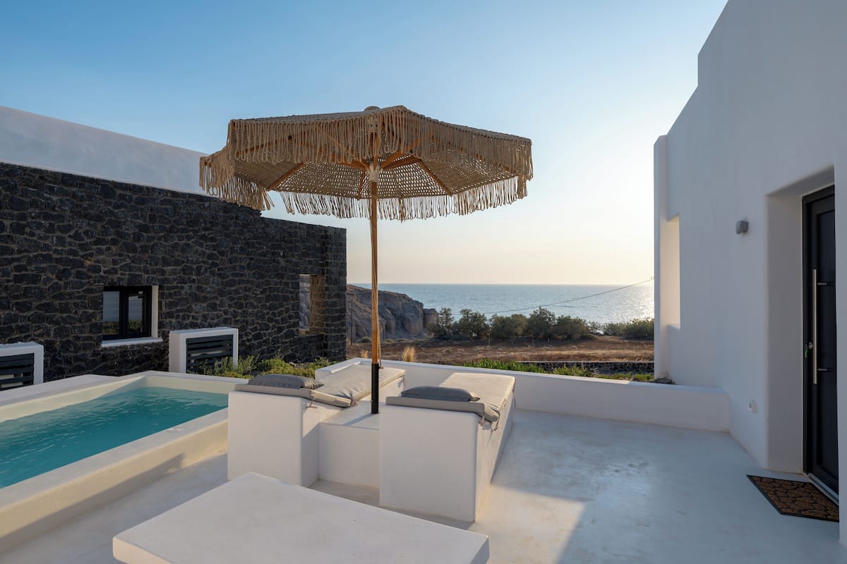 Un espace piscine extérieur moderne, agrémenté d’un mur en pierre, de chaises longues blanches et offrant une vue sur la mer.