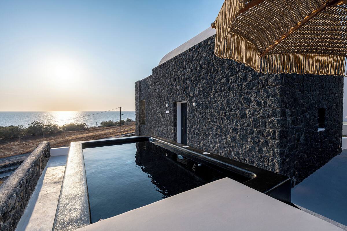 Un espace piscine moderne, avec un mur en pierre et une vue sur la mer au coucher du soleil.