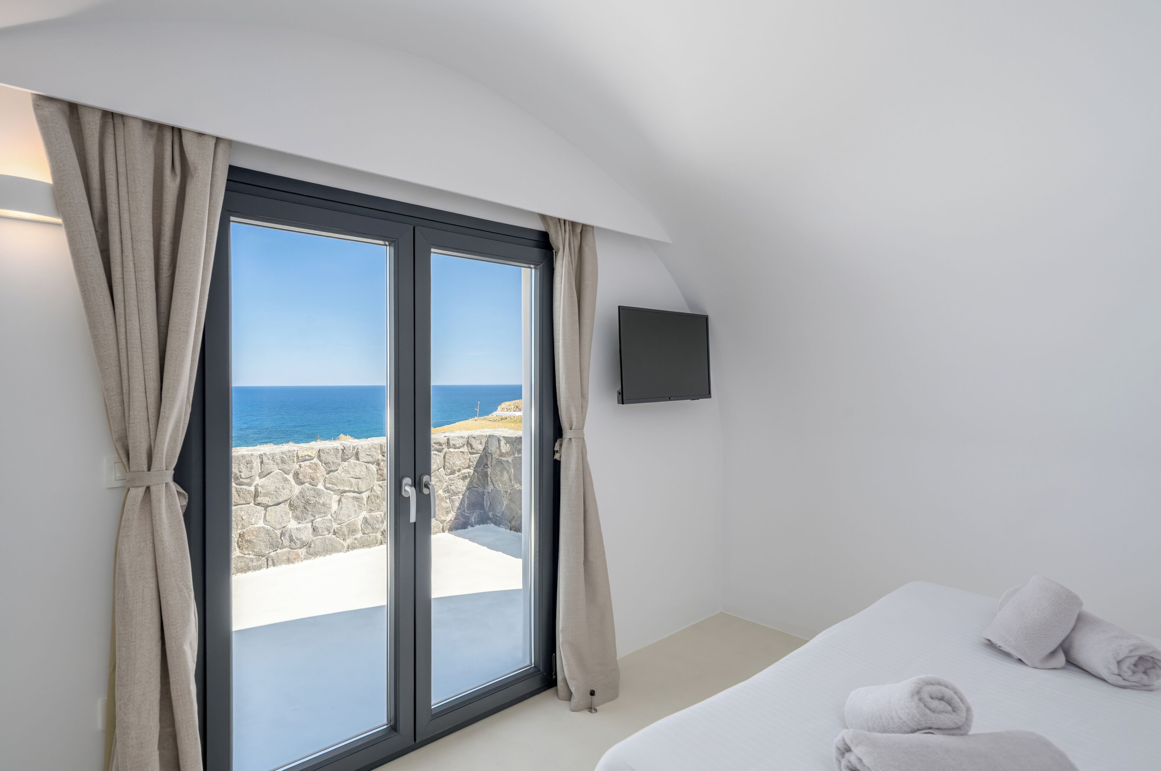 A bedroom with a large sliding glass door leading to a balcony with a stone wall and ocean view.