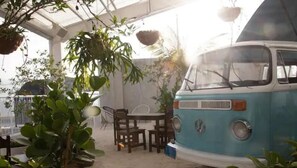 Relax in a serene garden setting, surrounded by lush greenery and potted plants, with a vintage van as a unique accommodation feature.