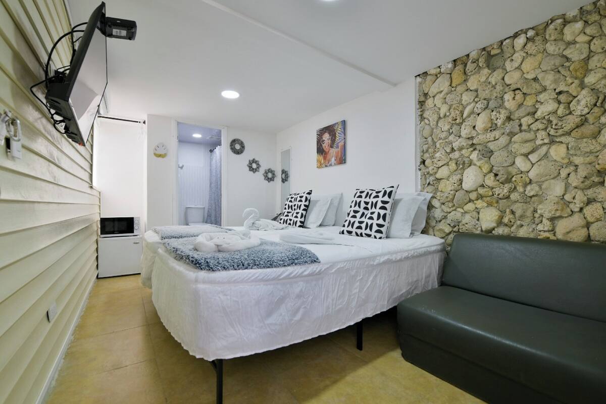 A bedroom with a bed, a gray couch, a stone wall, and a microwave.