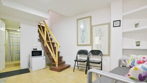 A compact living space with a staircase, a kitchenette, two chairs, and a bed with a floral pillow.