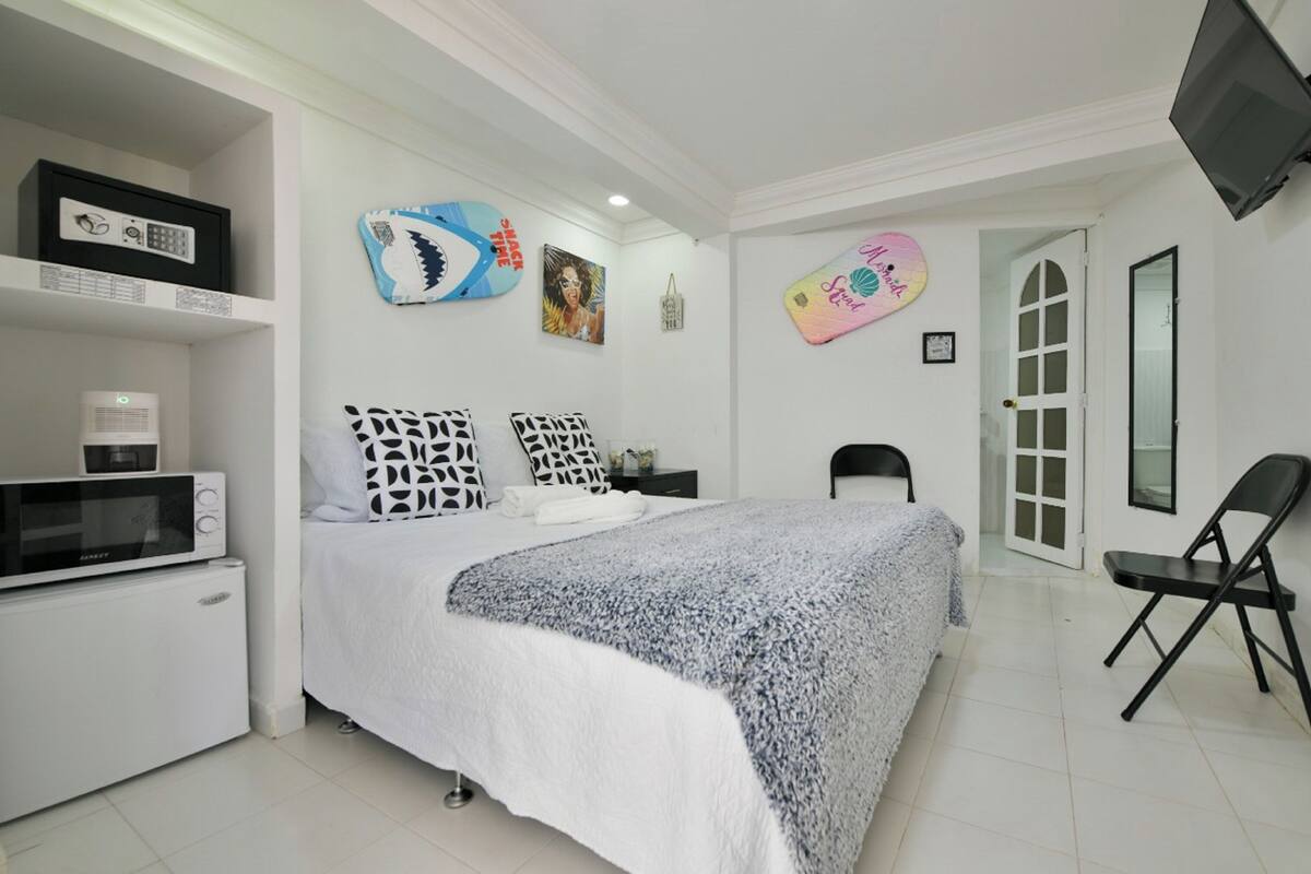 A bedroom with a bed, a TV mounted on the wall, a microwave, a small fridge, and a chair.