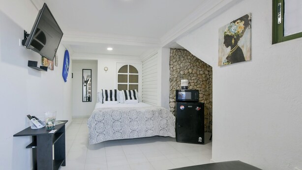A bedroom with a bed, a small desk, a TV, a microwave, and a refrigerator.
