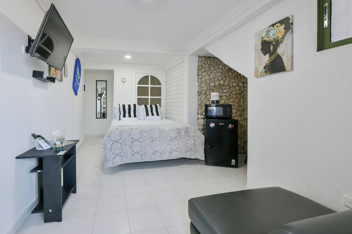 A bedroom with a bed, a small desk, a TV, a microwave, and a refrigerator.