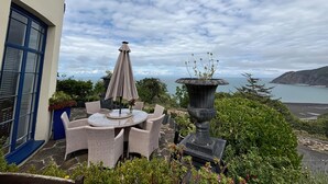 Een terras met rieten meubilair en een decoratieve vaas, met uitzicht op een kustlandschap.