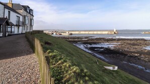 A coastal building with a gravel driveway and a wooden fence. - Dinguardi (Seahouses)