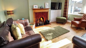 A living room with a fireplace, leather sofas, a television, and a window with curtains. - Dinguardi (Seahouses)