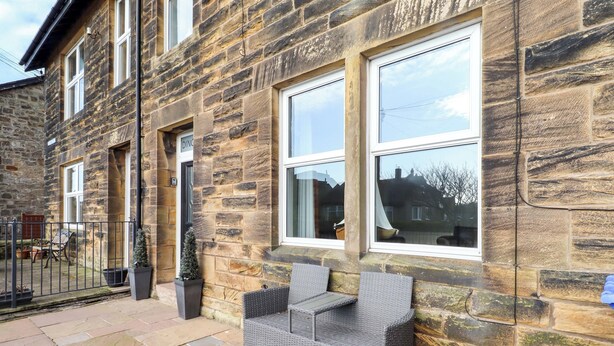 A stone building with a patio area featuring a wicker bench and potted plants. - Dinguardi (Seahouses)