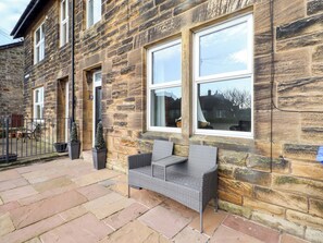 A stone building with a patio area featuring a wicker bench and potted plants. - Dinguardi (Seahouses)