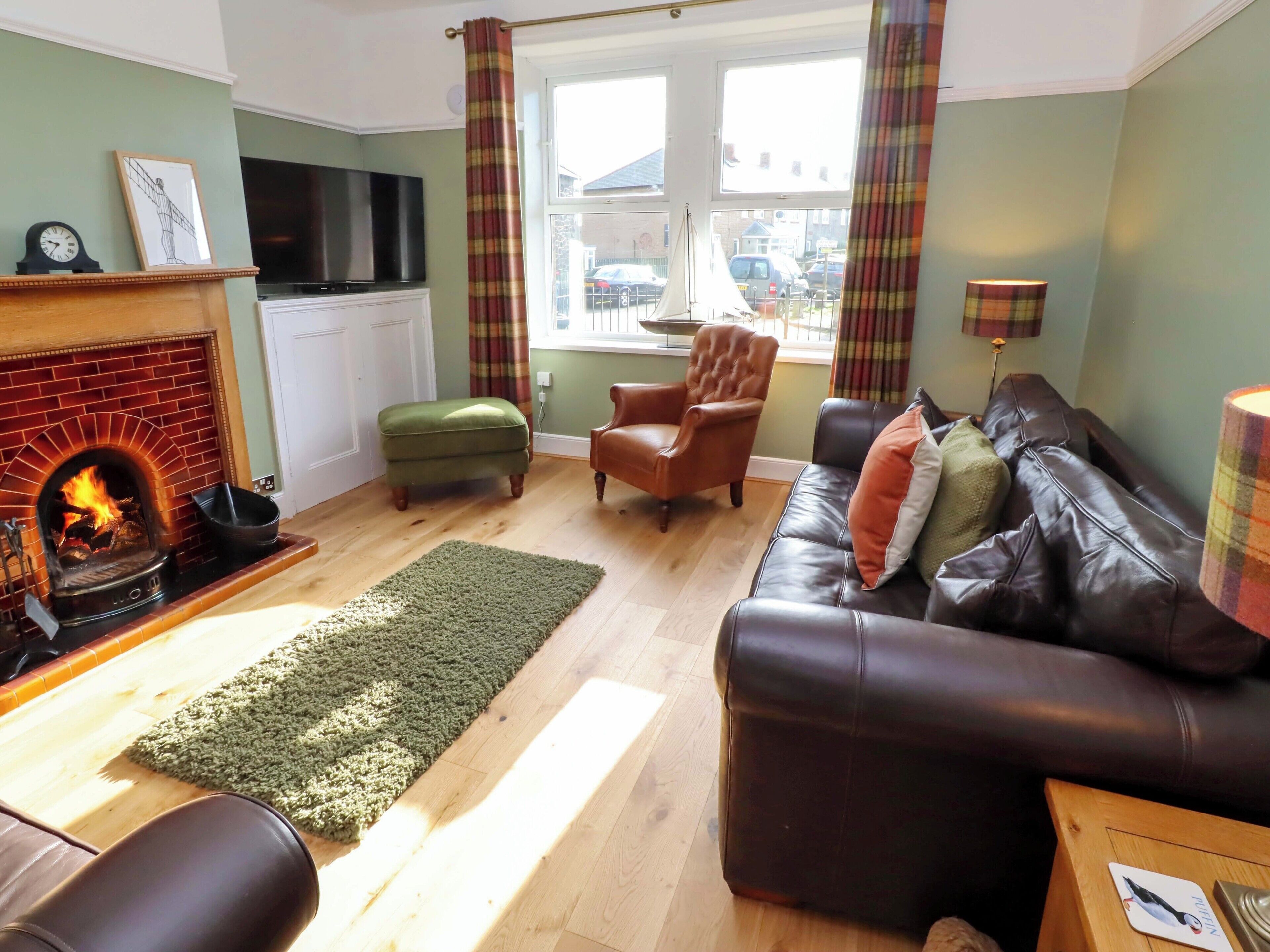 A living room with a fireplace, leather sofa, green armchair, and a TV mounted on the wall.