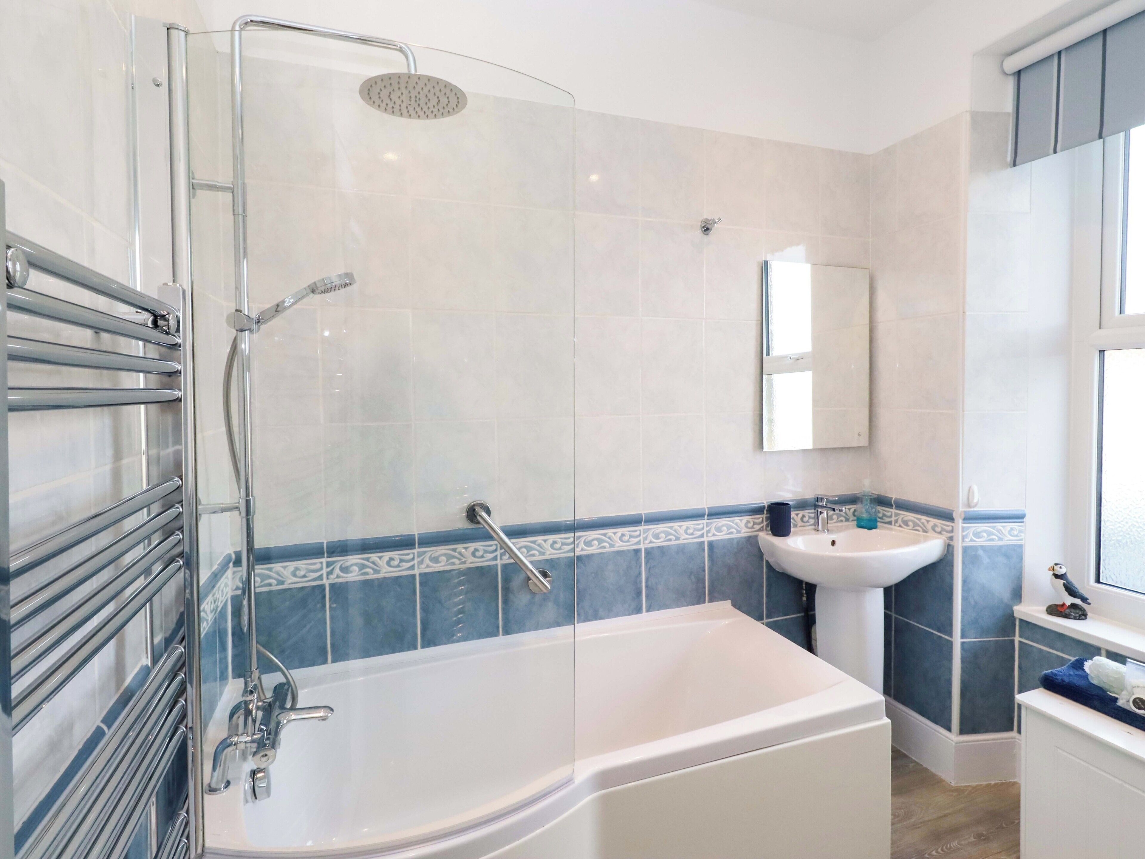 A modern bathroom with a glass-enclosed shower, a white bathtub, and a sink with a mirror above it.