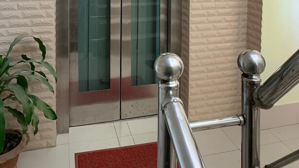 Un ascensor con pantalla digital, puerta de cristal y barandilla de metal.
