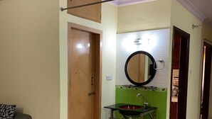 Un baño con puerta de madera, un lavabo verde con espejo y un felpudo rojo en el suelo.