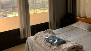 Habitación de hotel con cama, ventana con cortinas, equipo de aire acondicionado y vista al exterior.