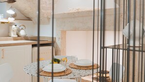 Un coin repas avec une table ronde dressée pour deux personnes, agrémentée d’assiettes blanches, d’un verre d’eau et d’une tasse jaune. La pièce est dotée d’un mur en pierre rustique et d’un plafond en bois.