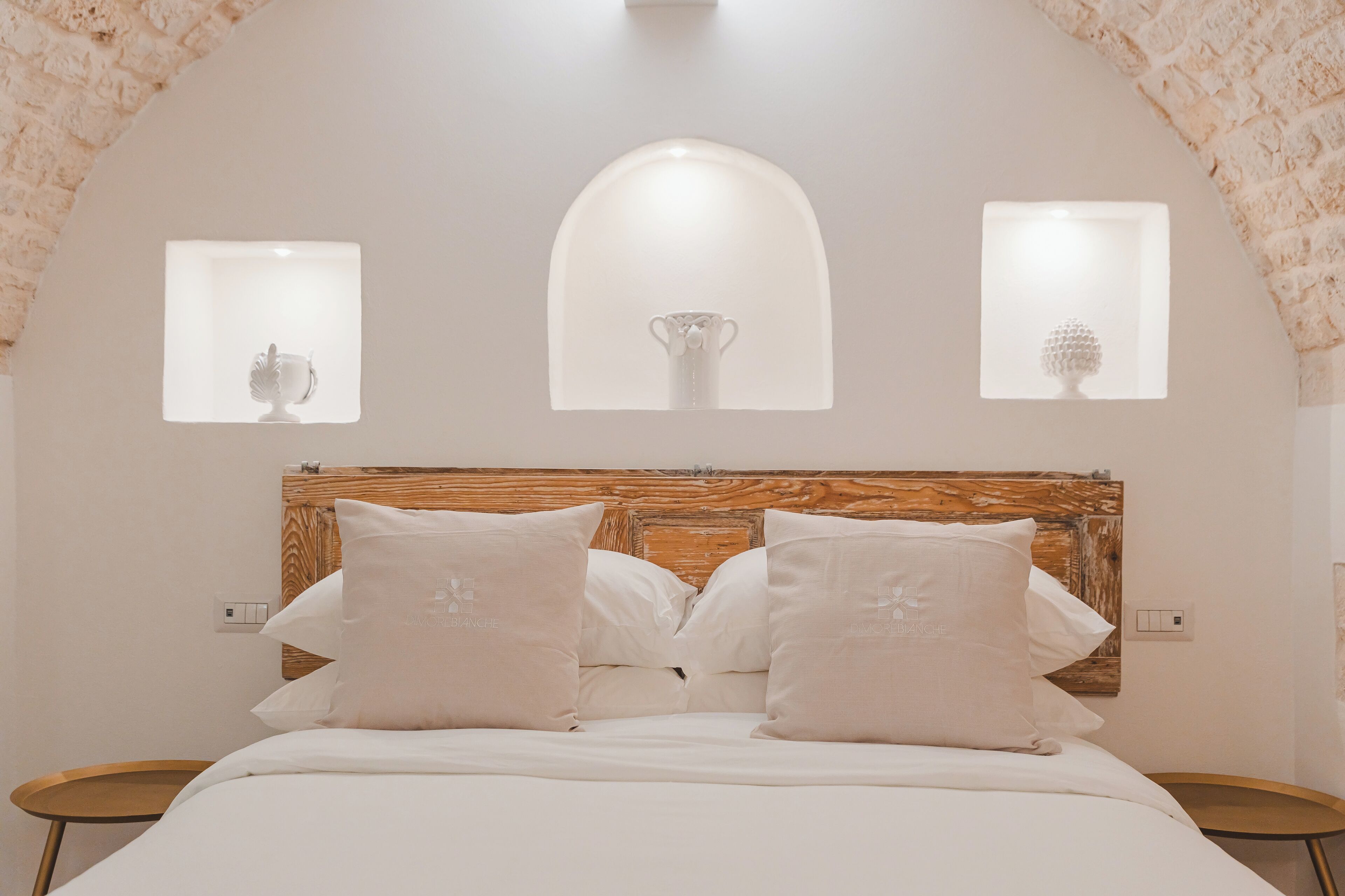 A bedroom with a wooden headboard, a bed with white linens, and three wall-mounted lights with decorative items.
