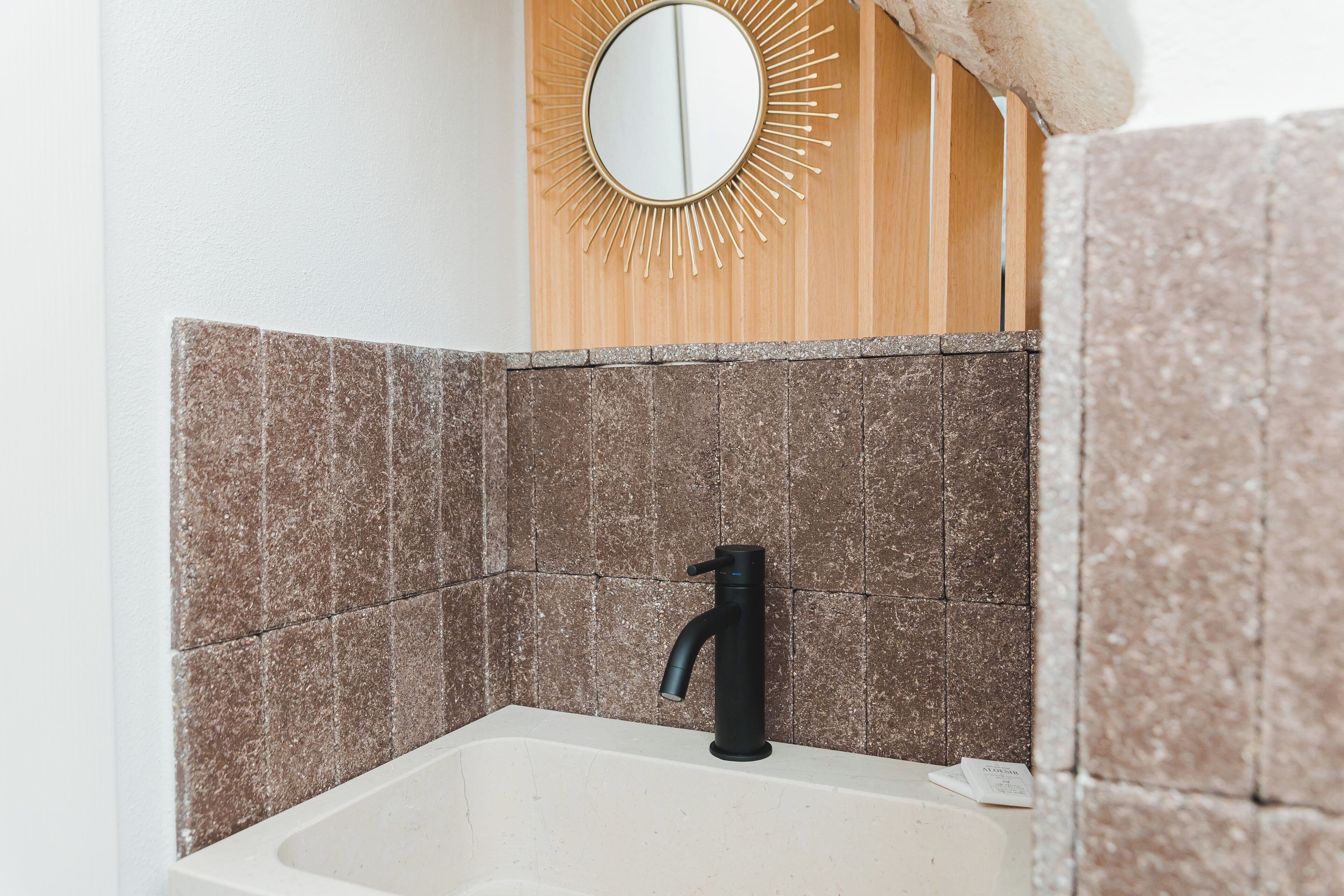 A bathroom with a white sink, a black faucet, and a mirror with a sunburst design on the wall.