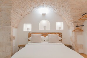 A bedroom with a stone arch ceiling, a wooden headboard, and a bed with white bedding. There are two bedside tables and a small round table. - Dimore Bianche L'Immacolata (Putignano)
